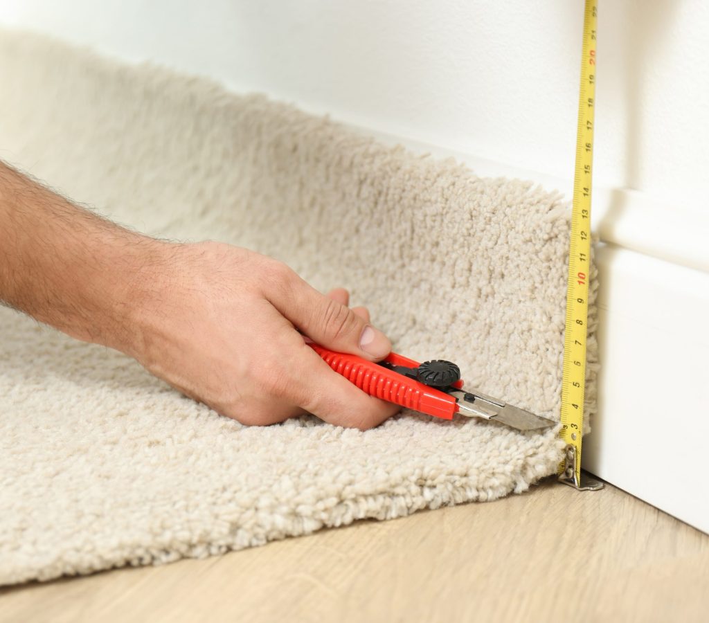Worker with cutter knife and measuring tape installing new carpet indoors, closeup